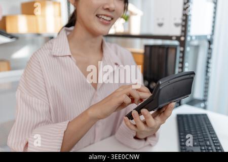 A young woman in a striped shirt works at her desk with documents, calculator, and smartphone, focusing on accounting tasks and financial planning for Stock Photo