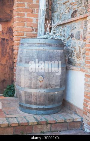 Wooden wine barrel leaning against a brick wall on a farm porch. The photo was taken near the seaside village of Rodia, Sicily, in Southern Italy Stock Photo