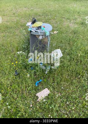 Cremona, Italy April 9th 2026 Overflowing waste bin in a grassy field with scattered trash highlighting environmental pollution and littering in a pub Stock Photo