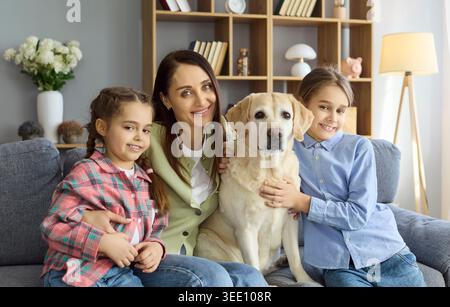 Happy mother with daughters and Labrador retriever on couch in bright living room Stock Photo