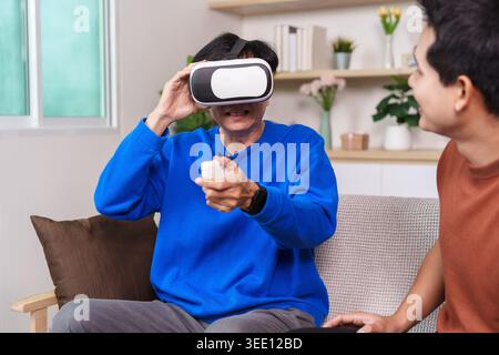 Asian senior man experiencing virtual reality with younger man at home Stock Photo