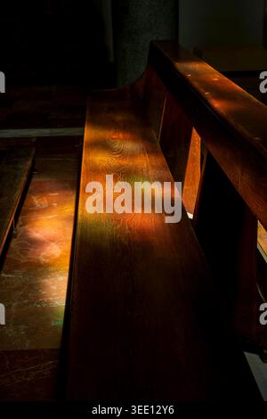 Colored light from a stained glass window illuminating a wooden pew in a church interior. Stock Photo