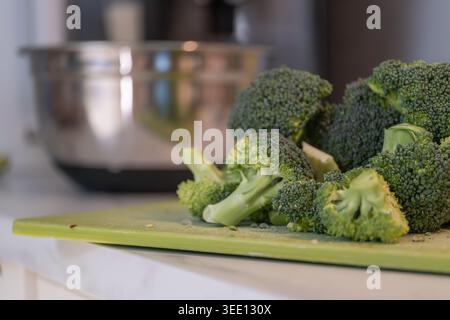 Fresh broccoli florets arranged on kitchen cutting board during home cooking process. Healthy eating and natural food preparation concept with green v Stock Photo