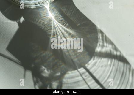 Abstract sunlight reflection created by glass object casting textured shadow and rainbow light patterns on white surface. Minimal artistic composition Stock Photo