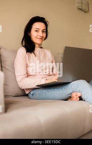 Cheerful female freelancer using computer at home on comfortable couch Stock Photo