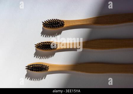 Bamboo toothbrushes on white surface in soft sunlight, minimal eco hygiene composition. Concept: Microplastic-free Stock Photo