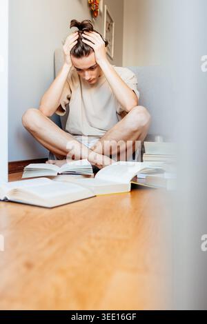 Stressed young person holding head while studying with open books Stock Photo
