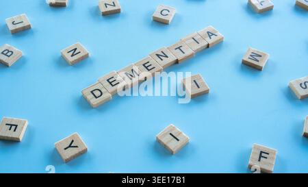 High angle view of wooden tiles spelling the word dementia at a diagonal angle over a blue backdrop with mixed alphabet letters Stock Photo