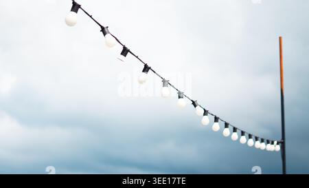 A string of round white light bulbs hanging against a cloudy blue sky. Stock Photo