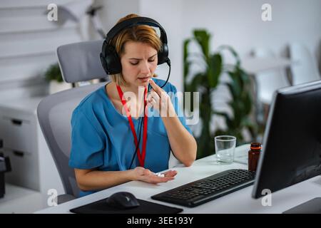 Healthcare worker wearing headset taking pills for headache or burnout during work Stock Photo