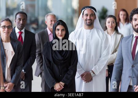 A diverse corporate team stands in a modern office, featuring Emirati leaders and professional colleagues smiling confidently, conveying teamwork, leadership, multicultural collaboration and business success. Stock Photo