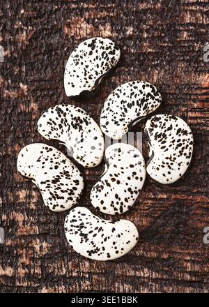 Flat lay of speckled lima beans (Phaseolus lunatus) on a dark wooden background. Group of raw organic butter beans. Stock Photo
