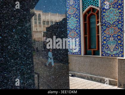 Reflection on a black marble wall of an local man walking near the Masjid Imam Ali A.S mosque in Bur Dubai, Dubai, UAE. Stock Photo