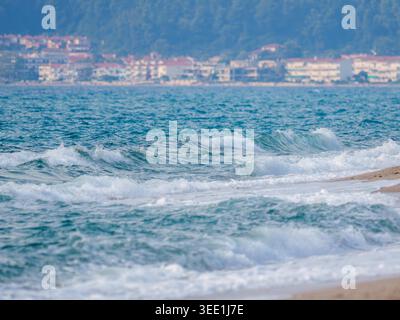 Blue-green sea waves breaking and rolling onto a sandy shoreline with white foam. Stock Photo