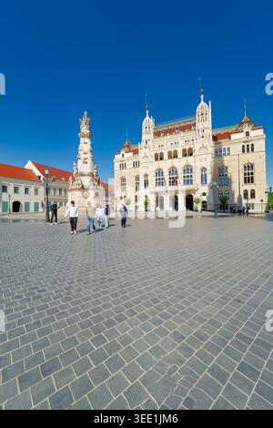 People walk in front of the Ministry of Interior building in Budapest. The sun shines brightly on the square and surrounding architecture. Stock Photo