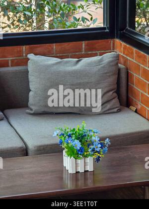 Gray cushion rests peacefully on cozy sofa beside red brick wall. beautiful green plant with small blue flower sits on wood table, providing perfectly Stock Photo