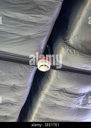 White smoke detector fire alarm mounted on ceiling near insulation duct providing reliable safety and security protection for commercial building agai Stock Photo