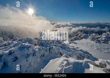 View of the snow-covered Salatin peak with frozen trees and a bright sun starburst over rolling clouds in Liptovska Stiavnica, Zilinsky kraj, Slovakia Stock Photo