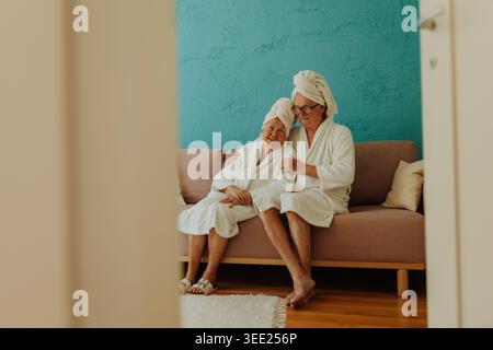 Portrait of happy senior couple sitting together in bathrobe on sofa. Stock Photo