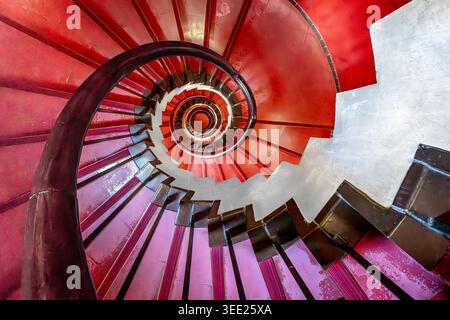 View of the vibrant red and pink spiral staircase of the Tokyo Metropolitan Art Museum with its elegant geometric curves and dark handrail in Taito Ci Stock Photo