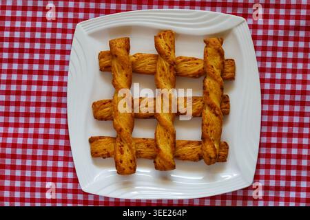 Cheese Twists all butter puff pastry with Gruyere cheese from M&S on plate on red and white checked gingham cloth Stock Photo