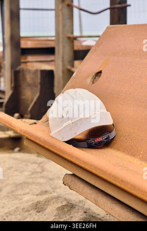 Health and Safety: Construction And Workplace Hazards White Hard Hat On Rusty Sheet Pile at construction site Stock Photo