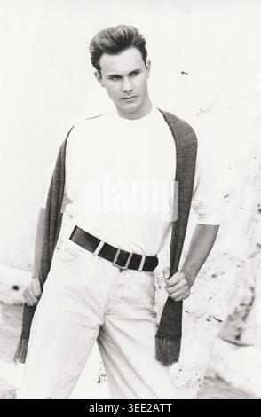 Black and white full-length portrait of a young male model standing confidently with a dark knitted scarf draped over his shoulders Stock Photo
