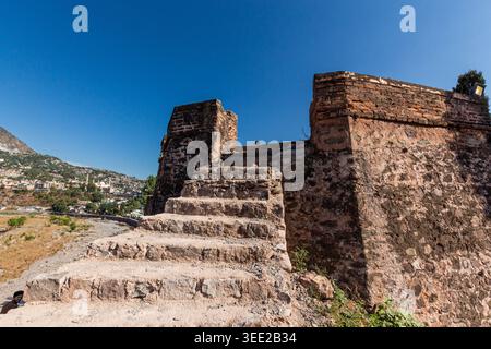 View of the stone stairs and ancient brick walls of the Red Fort Muzaffarabad with the city in the background under a clear blue sky in Muzaffarabad, Stock Photo