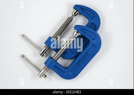 A studio photograph of two blue metal C-clamps with threaded steel screws, isolated on a white background, highlighting their industrial design and pr Stock Photo
