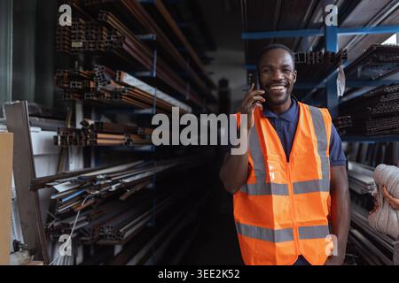 African American factory worker checks equipment and talking on phone in industrial setting. Stock Photo
