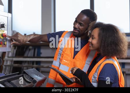 Two African American workers are collaborating in a factory while operating industrial machinery and managing production tasks. Stock Photo