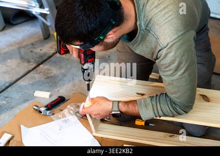 Horizontal shot of a man using a power drill to assemble wooden furniture, engaged in DIY home improvement, woodworking, and carpentry tasks Stock Photo