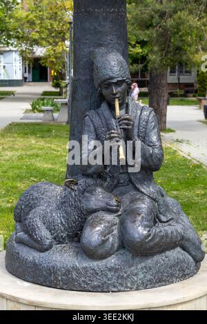 Bronze statue of a young shepherd playing flute with a lamb at his feet in a park Stock Photo
