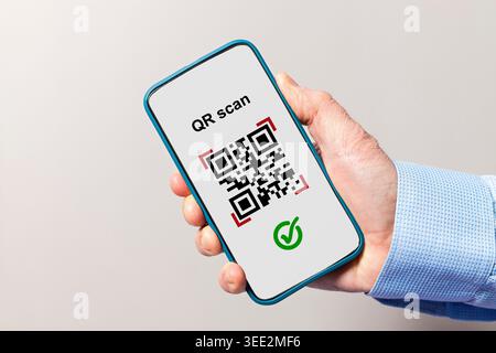 Hand holding smartphone scanning a qr code with a green checkmark indicating successful verification Stock Photo