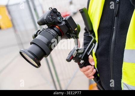 Videographer using a digital camera with a large lens and electronic steadycam system for high quality content production at a construction facility w Stock Photo