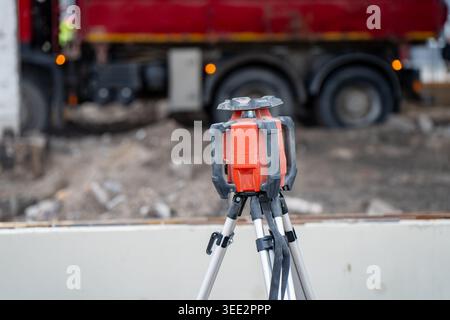 Surveying laser level standing on tripod at construction site with truck in background, useful for building layout and measurement workflow today Stock Photo
