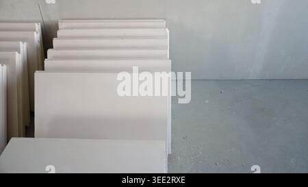 Minimalist composition of stacked white gypsum boards on gray concrete floor. Unfinished room at construction site with building materials ready for i Stock Photo
