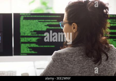 Female software developer coding at computer with dual monitors in modern office Stock Photo