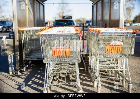Rows of metal shopping carts with orange handles parked in a designated shelter at a supermarket parking lot, representing retail consumerism and groc Stock Photo