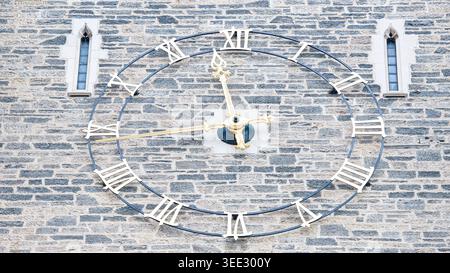 Close view of Soldiers Tower clock with golden hands and Roman numerals set against textured stone wall with narrow vertical windows. Stock Photo