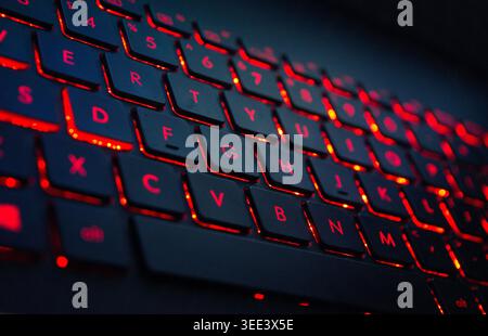 Modern laptop with vibrant RGB keyboard with red lighting on a dark desk, showcasing gaming tech, performance, and sleek contemporary design. Stock Photo