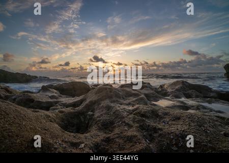 View of the sun setting over a rocky coastline with waves crashing against the shore in Florida, United States. Stock Photo