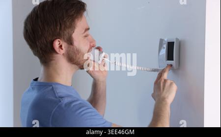 Man with handset pressing button on intercom panel indoors Stock Photo