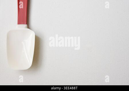 Red handle spatula placed on a clean white table with a minimalist and modern composition. Perfect for concepts related to cooking, baking, kitchen Stock Photo