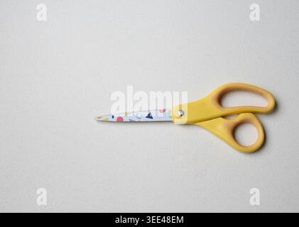 Yellow handle scissors placed on a clean white table with a minimalist composition and sharp detail. Perfect for concepts related to office supplies, Stock Photo