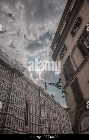 An upward-looking photo capturing the intricate details of a historic building facade in Florence, Italy, contrasted against a cloudy sky with sunligh Stock Photo