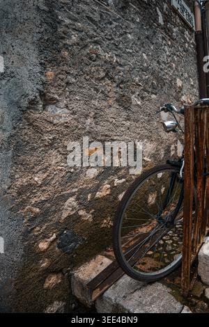 A close-up view of a vintage bicycle wheel leaning against a weathered and textured stone wall in Catania, Sicily. The image captures the rustic charm Stock Photo