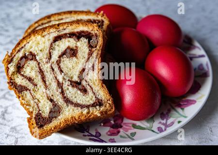 A plate featuring a slice of swirled bread and four dyed red eggs, likely for Easter celebration. Stock Photo