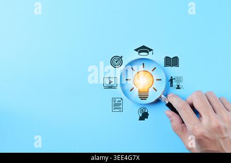 Creative learning idea and education innovation concept, hand holding magnifying glass over light bulb with icons for online course, book, graduation, Stock Photo