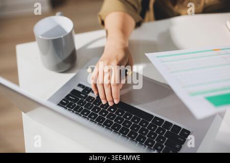 Young Asian woman working late at her desk, having a video call or online meeting with a laptop, analyzing data and managing business financials in an Stock Photo